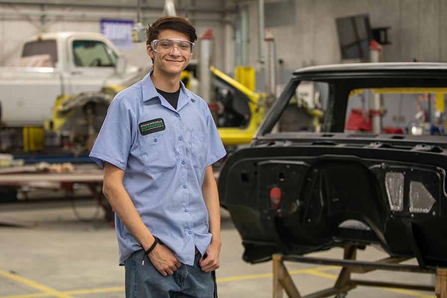 San Juan College student standing in front of a car frame in the auto body shop