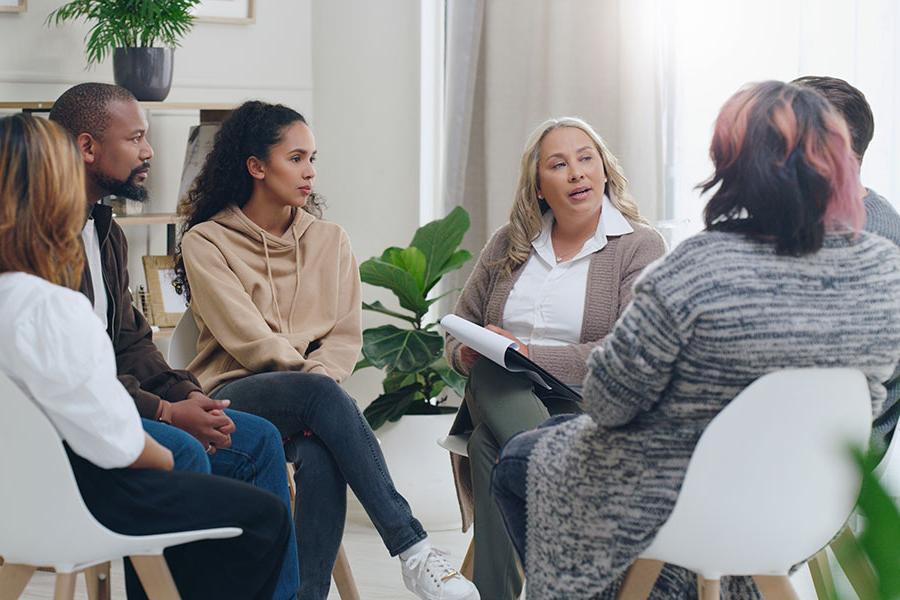 A therapist leading a group counseling session with a diverse group of people sitting in a circle